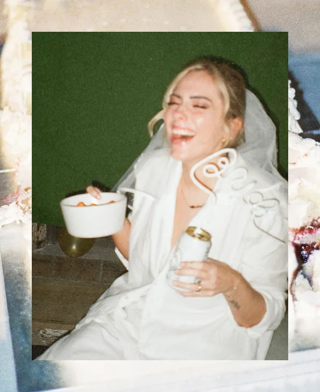 A laughing bride in a white robe holding a drink.