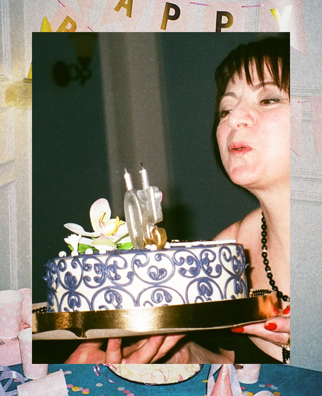 A woman blowing out candles on a decorated blue and gold cake.