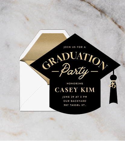 A black and gold graduation party invitation shaped like a mortarboard, paired with a white envelope with a gold foil lining.